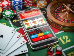 Casino online. Smartphone or mobile phone, slot machine, dice, cards and roulette on a green table in casino.